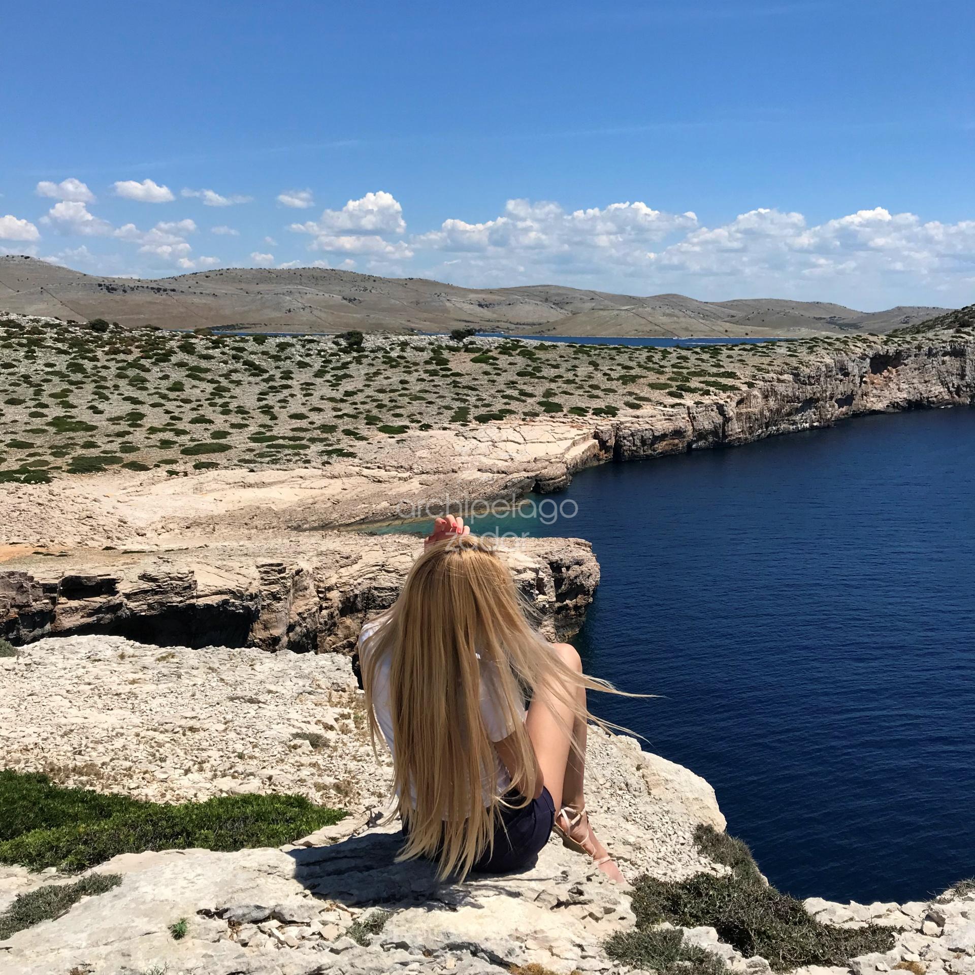 girl on a cliff on mana island looking pam+noramic views on kornati